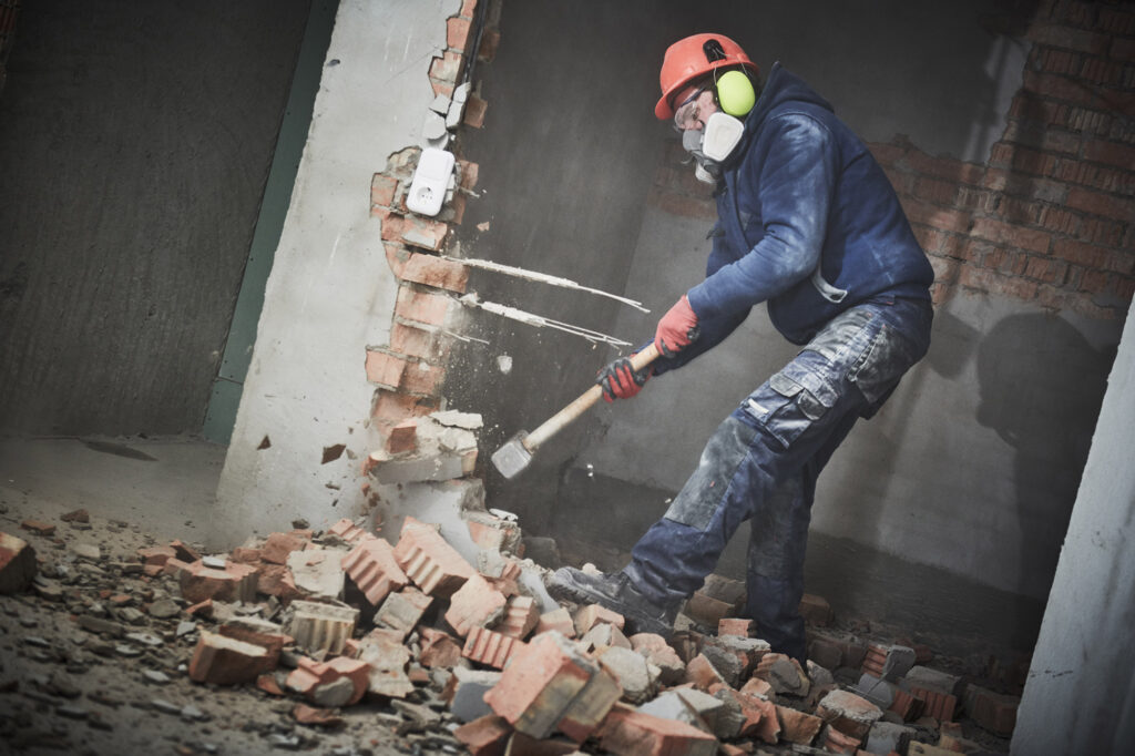 Arbeider met helm en mondmasker breekt een bakstenen muur af