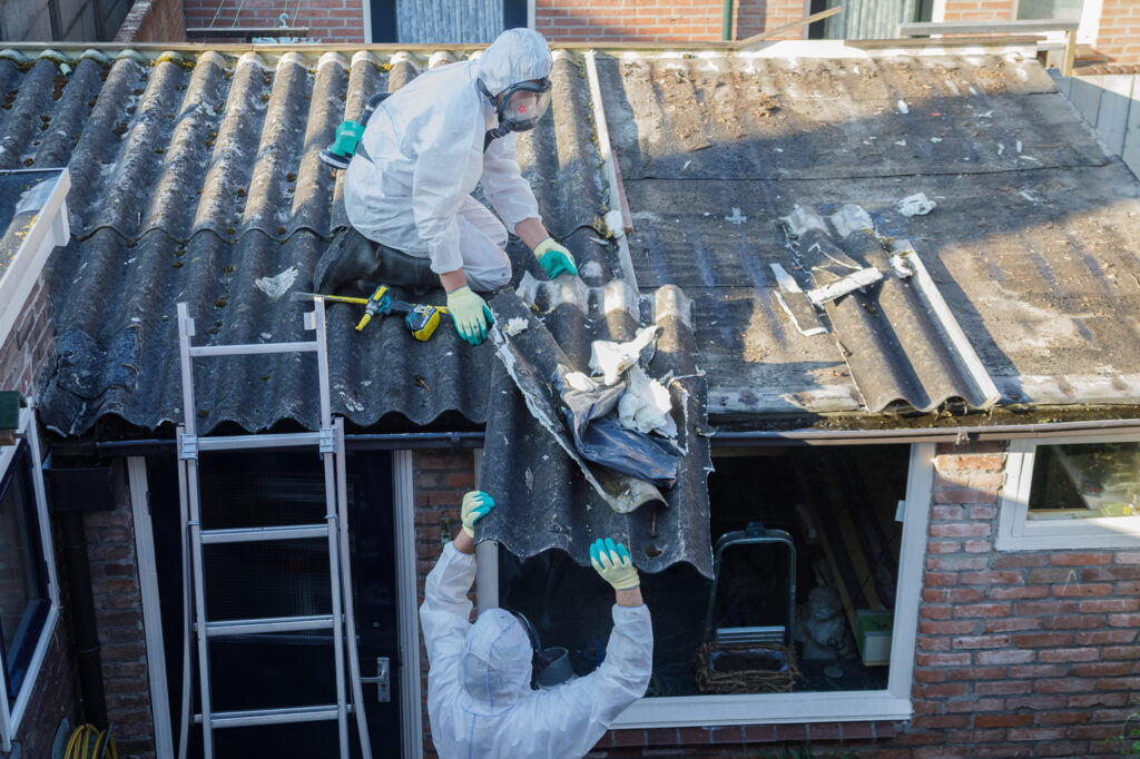 Asbestverwijderaars in beschermende pakken halen golfplaten van een dak